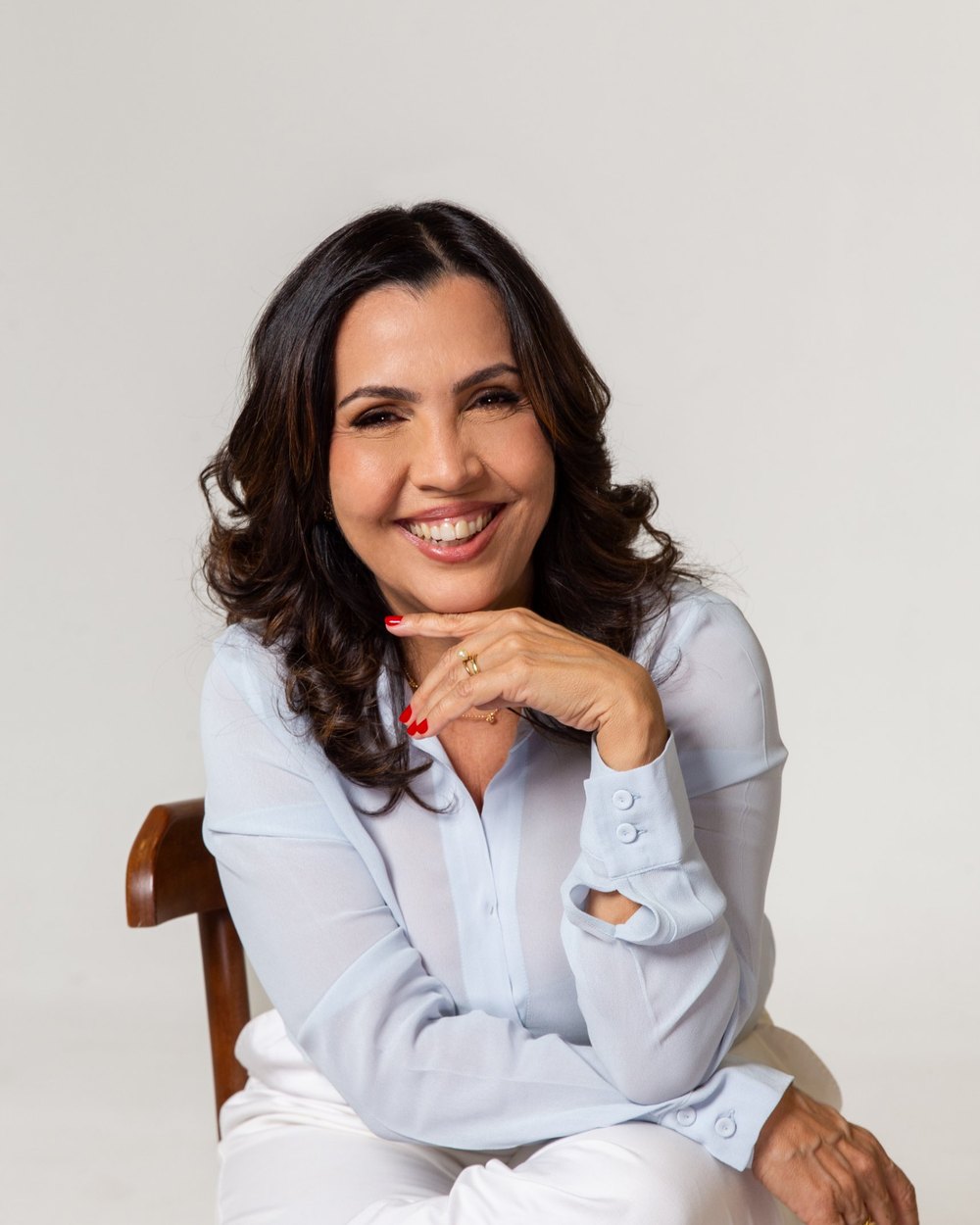 Tatiana Teixeira sorrindo, de blusa azul-clara, com a mão no queixo