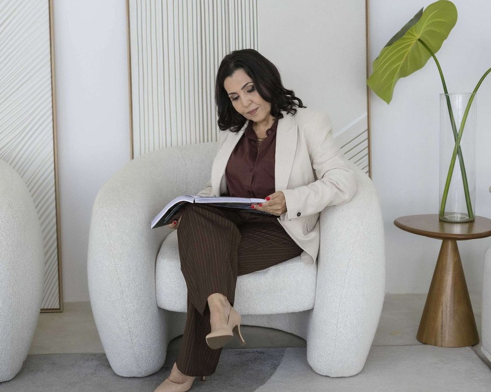 Tatiana Teixeira sentada em uma poltrona clara, lendo